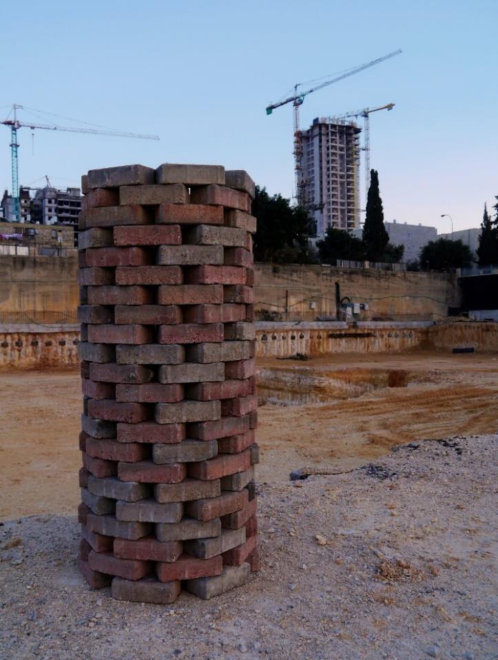 The brick column close up against a pale sky, construction cranes rising behind the excavated site.