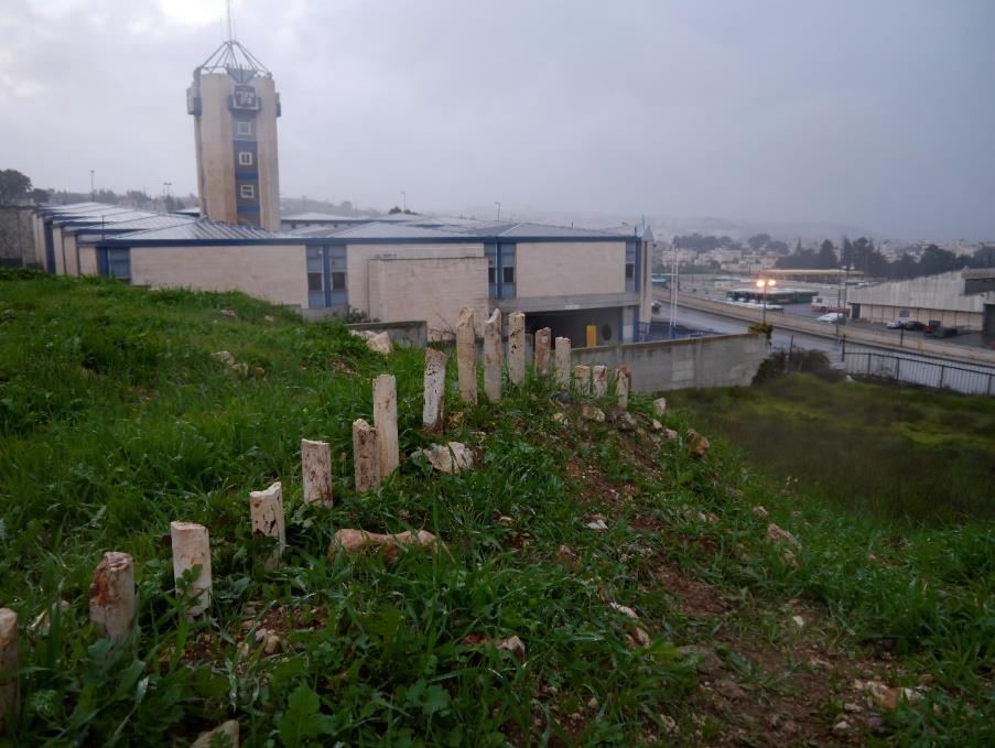 Pale limestone blocks set in a long line across a green hillside, a low building and tower behind under grey cloud.