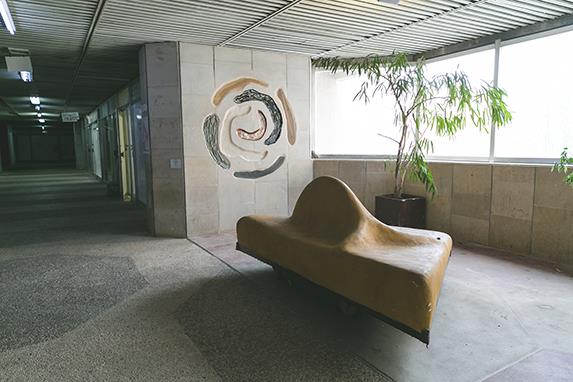 The spiral relief seen along a daylit corridor of the Clal building, a curved bench beneath it.